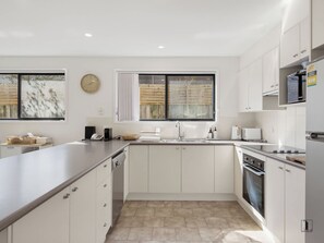 A modern kitchen with white cabinetry, a large island, a built-in oven, and a window with curtains. - Seaside Living, Steps to the Beach (LONG BEACH)