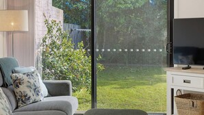 A living room with a sofa, a TV, and a sliding glass door leading to a garden. - Seaside Living, Steps to the Beach (LONG BEACH)