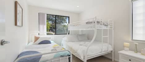 Un dormitorio con literas, una cama individual, una mesita de noche y un ventanal con vistas a árboles.