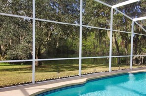 Piscina cercada por um muro branco, com vista para árvores e gramado.