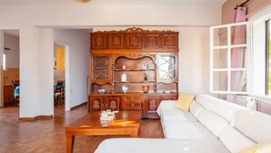 Un salon avec un canapé blanc, un meuble en bois doté de portes en verre, et un coin repas à l’arrière-plan.