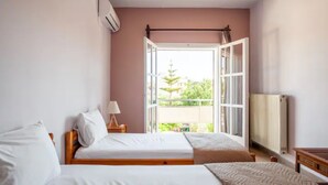 Une chambre avec deux lits, une fenêtre avec une porte ouverte, un radiateur et une lampe sur une table de chevet.