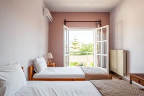 Une chambre avec deux lits, une fenêtre avec une porte ouverte, un radiateur et une lampe sur une table de chevet.