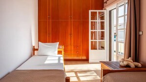 Une chambre d’hôtel avec un lit, une petite table sur laquelle est posé un ours en peluche, une armoire et une porte-fenêtre coulissante donnant sur un balcon.