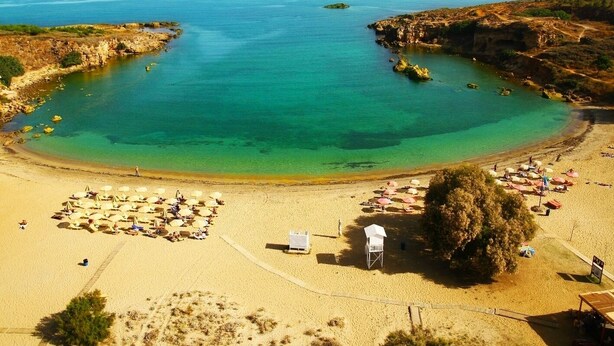 Une plage aux eaux turquoise et limpides, avec un rivage sablonneux et des parasols.