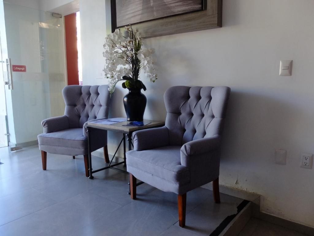 Dos sillones tapizados en gris con patas de madera, una mesita y un florero con flores blancas.
