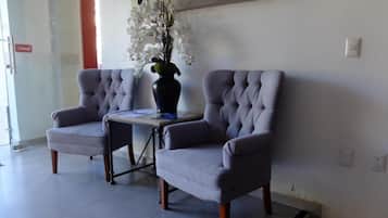 Dos sillones tapizados en gris con patas de madera, una mesita y un florero con flores blancas.