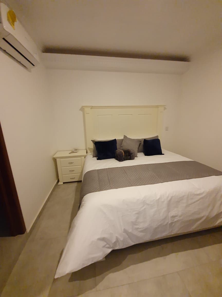 Habitación individual con una cama de somier blanco, una mesita de noche con cajones, edredón blanco y manta gris.