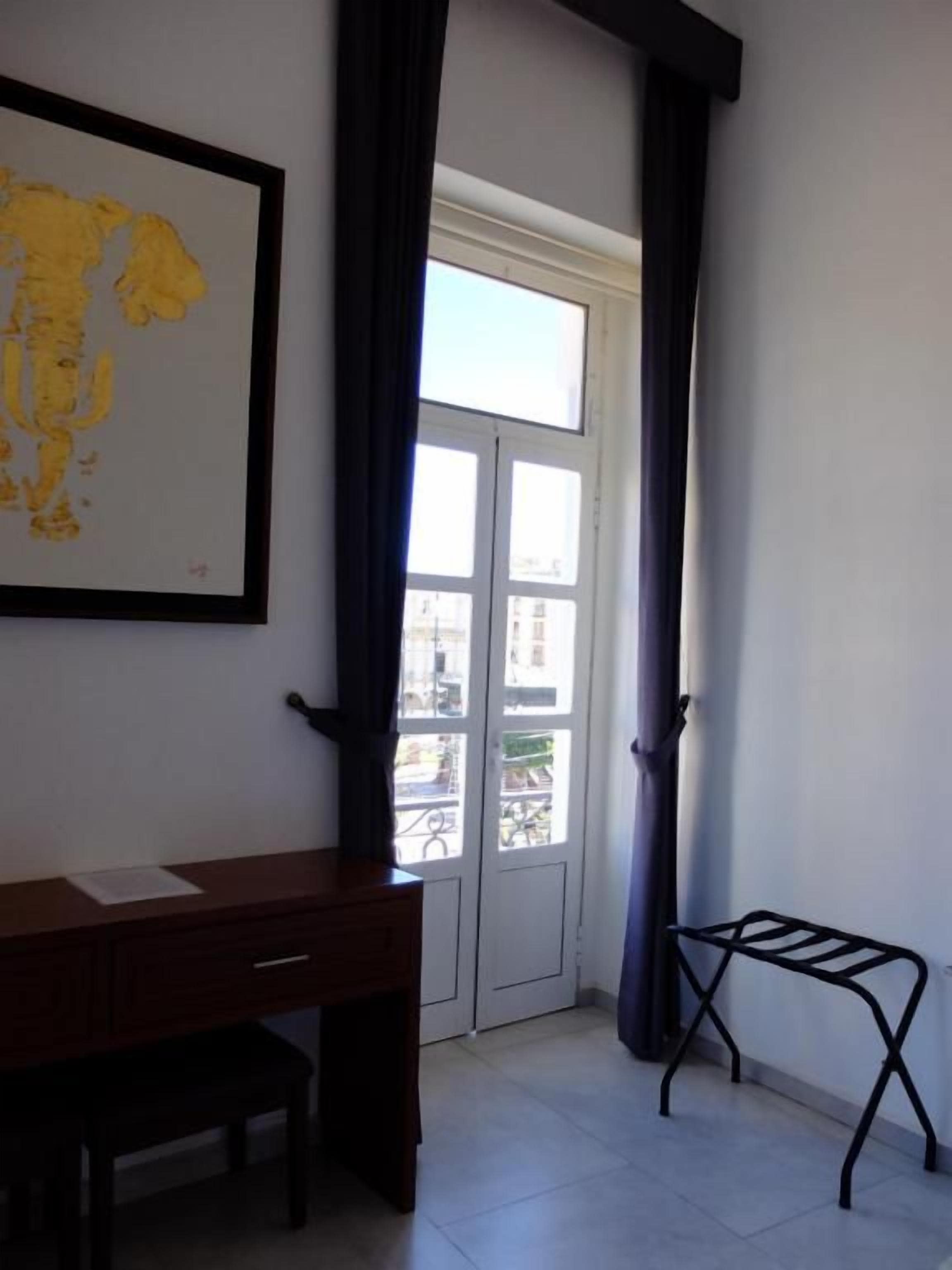 A room with a desk, a chair, a window with curtains, and a metal drying rack.