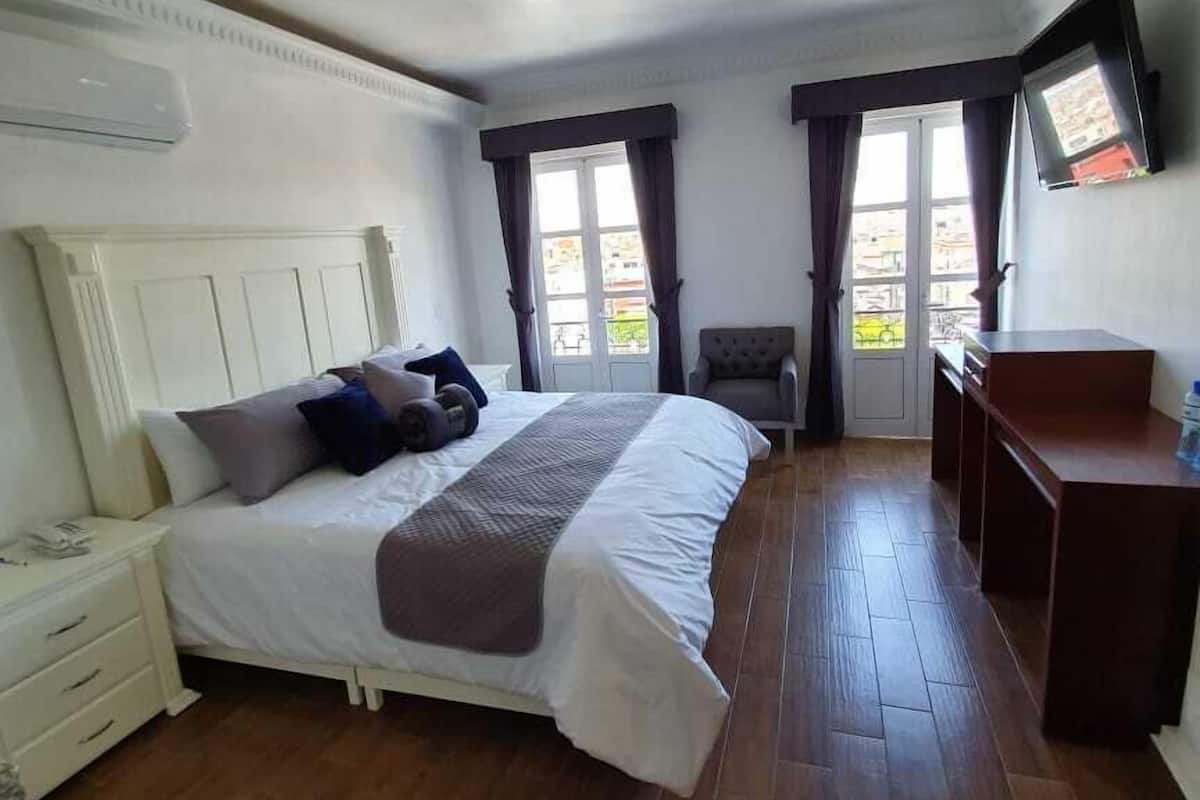 A bedroom with a bed, bedside table, and a flat-screen TV mounted on the wall.