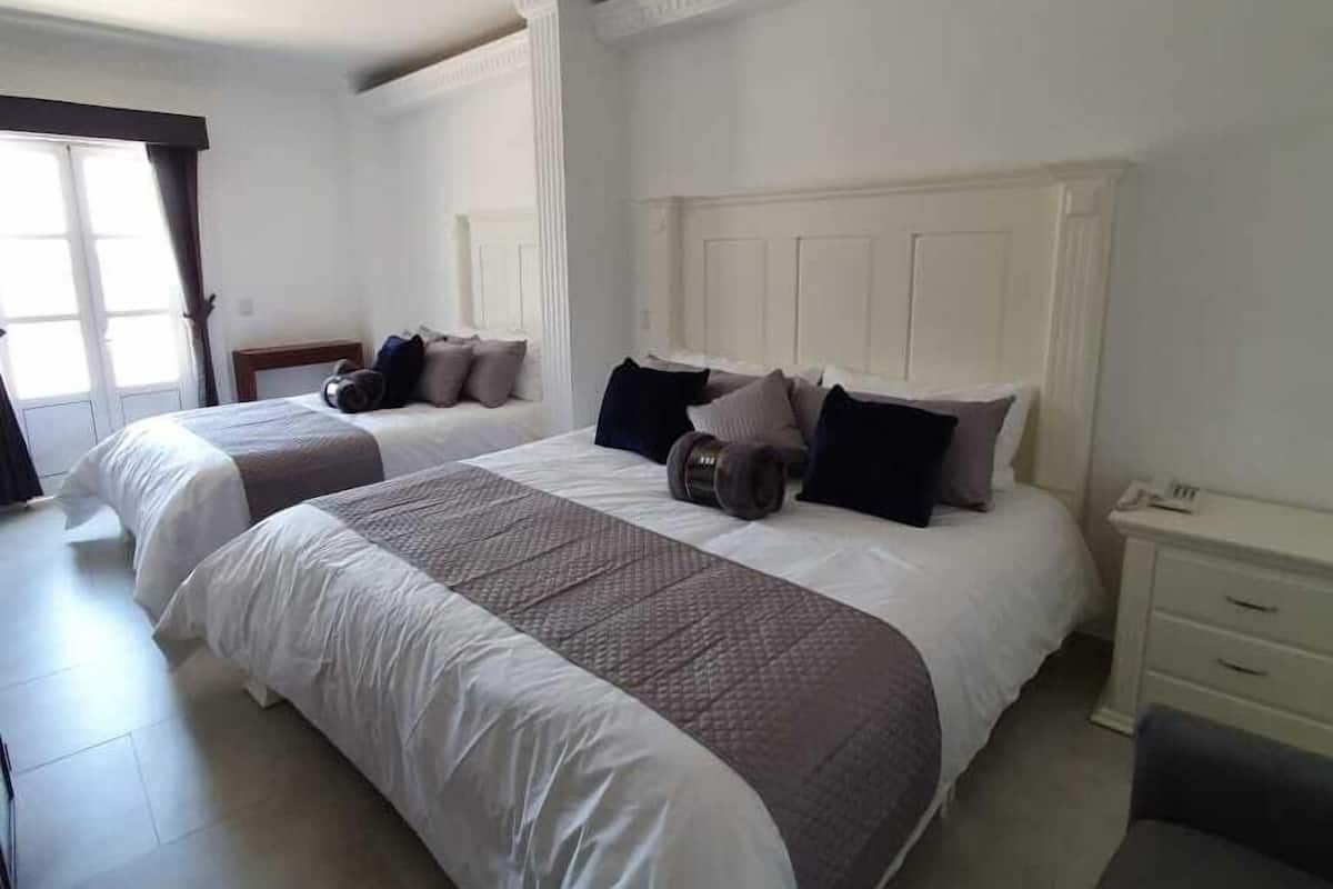 A hotel room with two beds, a nightstand, and a chair.