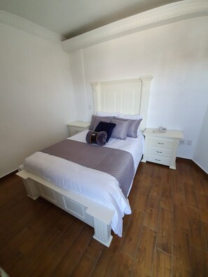 A bedroom with a bed, nightstands, and a wooden floor. - Hotel Estancia Real (Tepatitlan de Morelos)