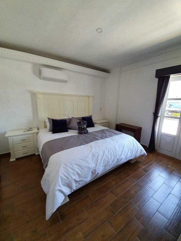 Un dormitorio con cama, mesita de noche, cómoda y ventana con cortinas.