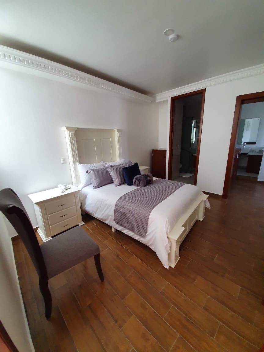 A bedroom with a bed, bedside table, chair, and a mirror.