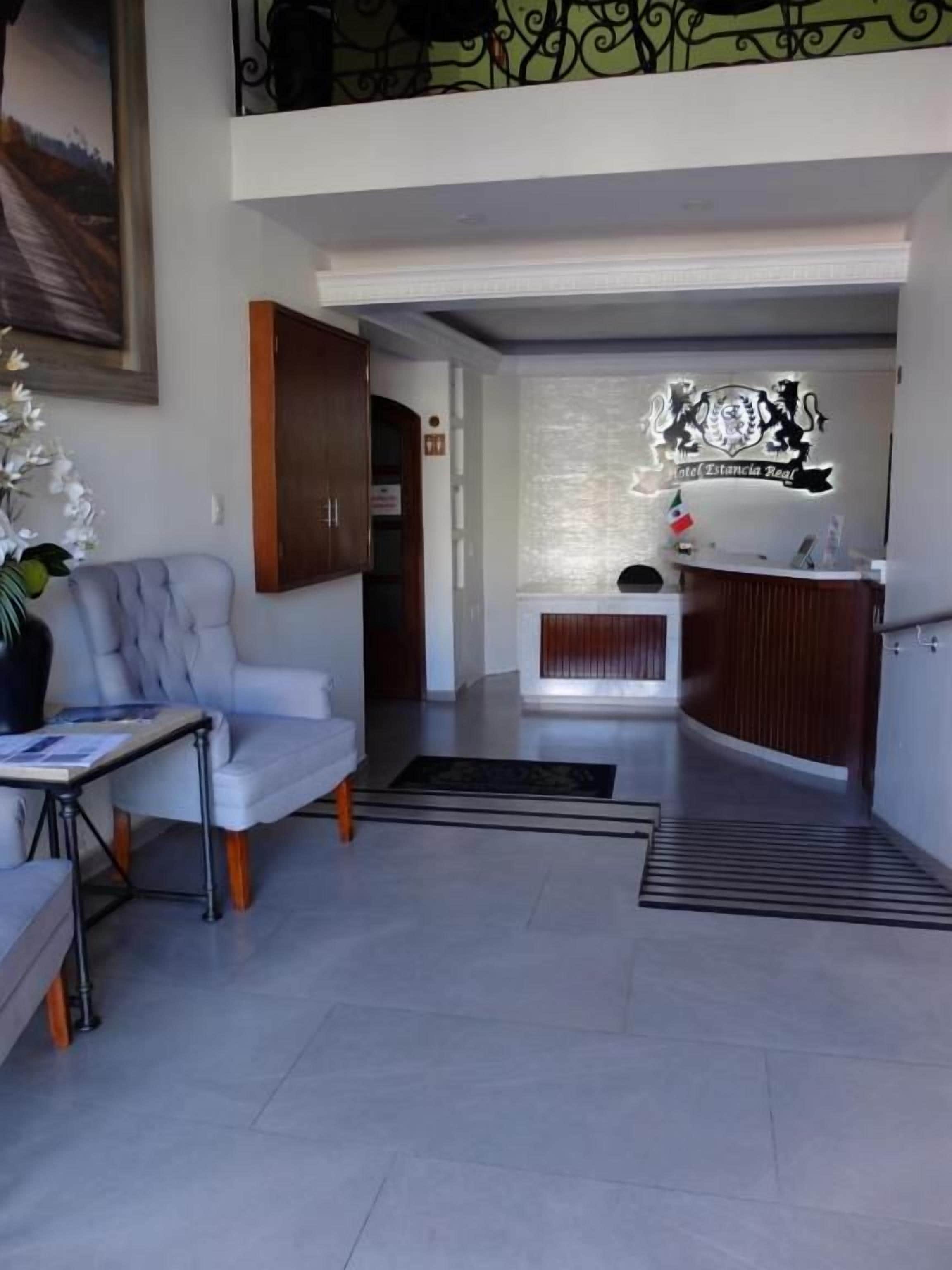 Een hotel lobby met een receptiebalie, een zithoek met een bank en een tafel, en een trap naar een hoger gelegen verdieping.