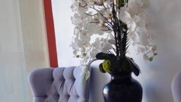 Un'area d'attesa con una poltrona trapuntata, un tavolino con un vaso di fiori bianchi e un quadro incorniciato sopra il tavolo.