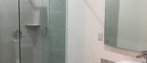 Un baño moderno con cabina de ducha de vidrio, un lavabo blanco y un espejo grande.