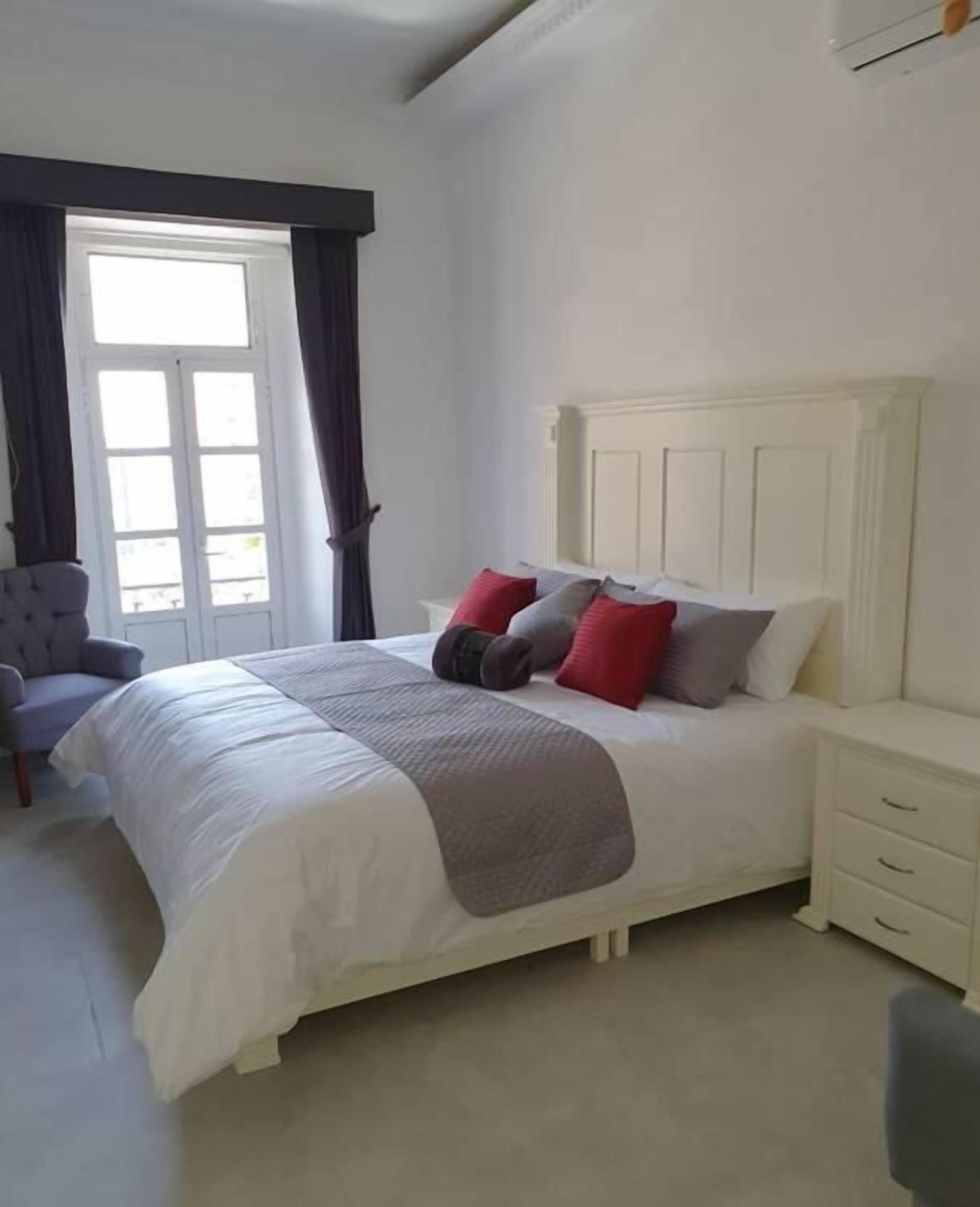 A bedroom with a bed, a nightstand, a chair, and a window with curtains.