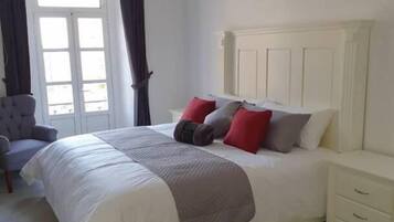 A bedroom with a bed, a nightstand, a chair, and a window with curtains.