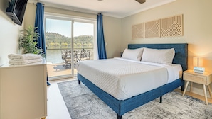 A bedroom with a bed, a TV mounted on the wall, a ceiling fan, and a view of a lake through a sliding door. - Lakefront Retreat w/ Kayaks, Paddle Boards & Deck! (Nine Mile Falls)