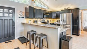 A modern kitchen with dark cabinetry, stainless steel appliances, and a bar area with stools. - Lakefront Retreat w/ Kayaks, Paddle Boards & Deck! (Nine Mile Falls)