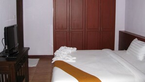 Quarto de hotel com uma cama grande, um guarda-roupa de madeira, uma televisão sobre uma cômoda de madeira e um tapete branco.