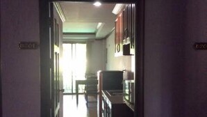 Um corredor estreito com piso de madeira que leva a uma área de cozinha com armários e geladeira.