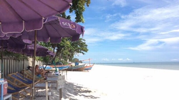 Uma praia com guarda-sóis, espreguiçadeiras e alguns barcos na água.