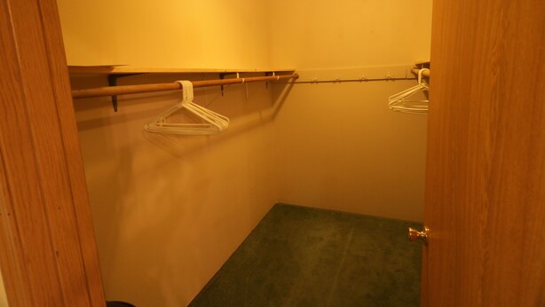 A small, narrow walk-in closet with wooden doors, a ceiling light, and a single metal hanger on a rod. - Alaska Dreamin' Lodging (Seward)
