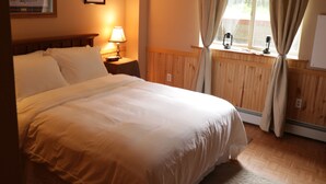 A hotel room with a large bed, a nightstand with a lamp, a window with curtains, and a framed picture on the wall. - Alaska Dreamin' Lodging (Seward)