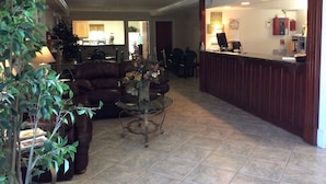 A reception area with a desk, chairs, and a coffee table. There is a couch and a plant in the foreground.