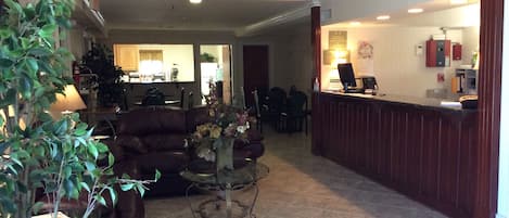 A reception area with a desk, chairs, and a coffee table. There is a couch and a plant in the foreground.