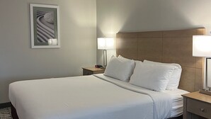 A hotel room with a large bed, two bedside tables with lamps, a headboard, a framed picture on the wall, and a patterned carpet.