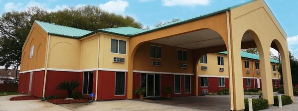 A multi-story hotel with a yellow and red facade, a covered entrance, and a parking area.
