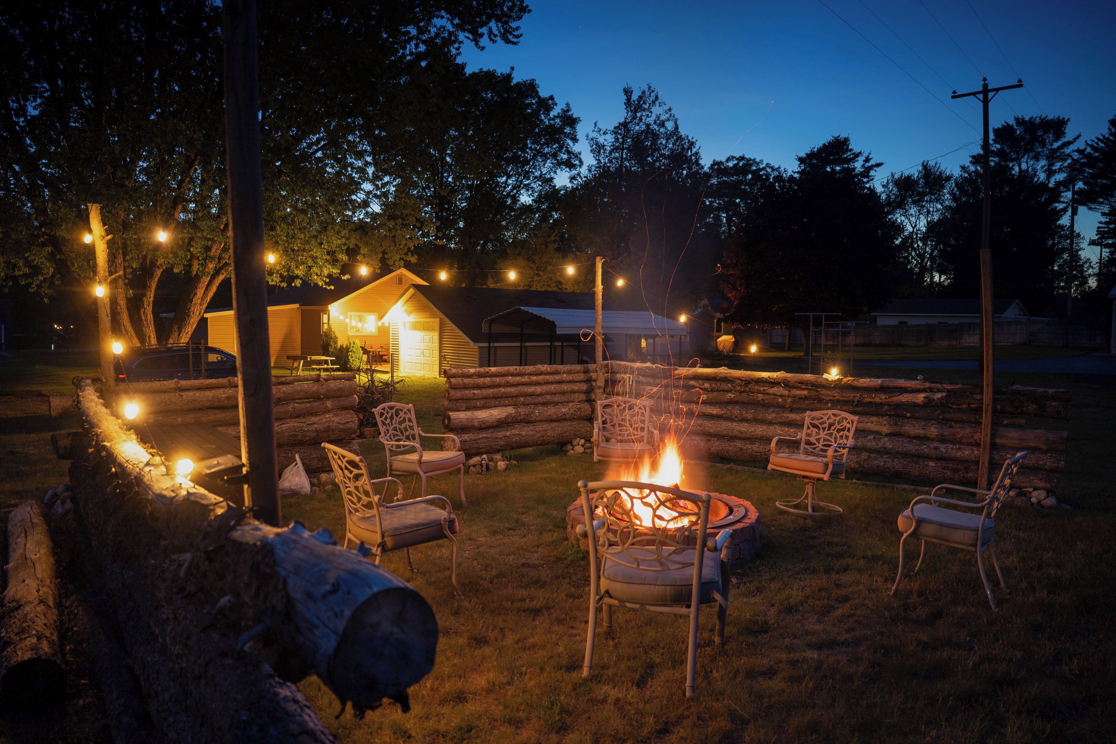 A log cabin with a fire pit and outdoor seating, surrounded by trees and a clear sky.