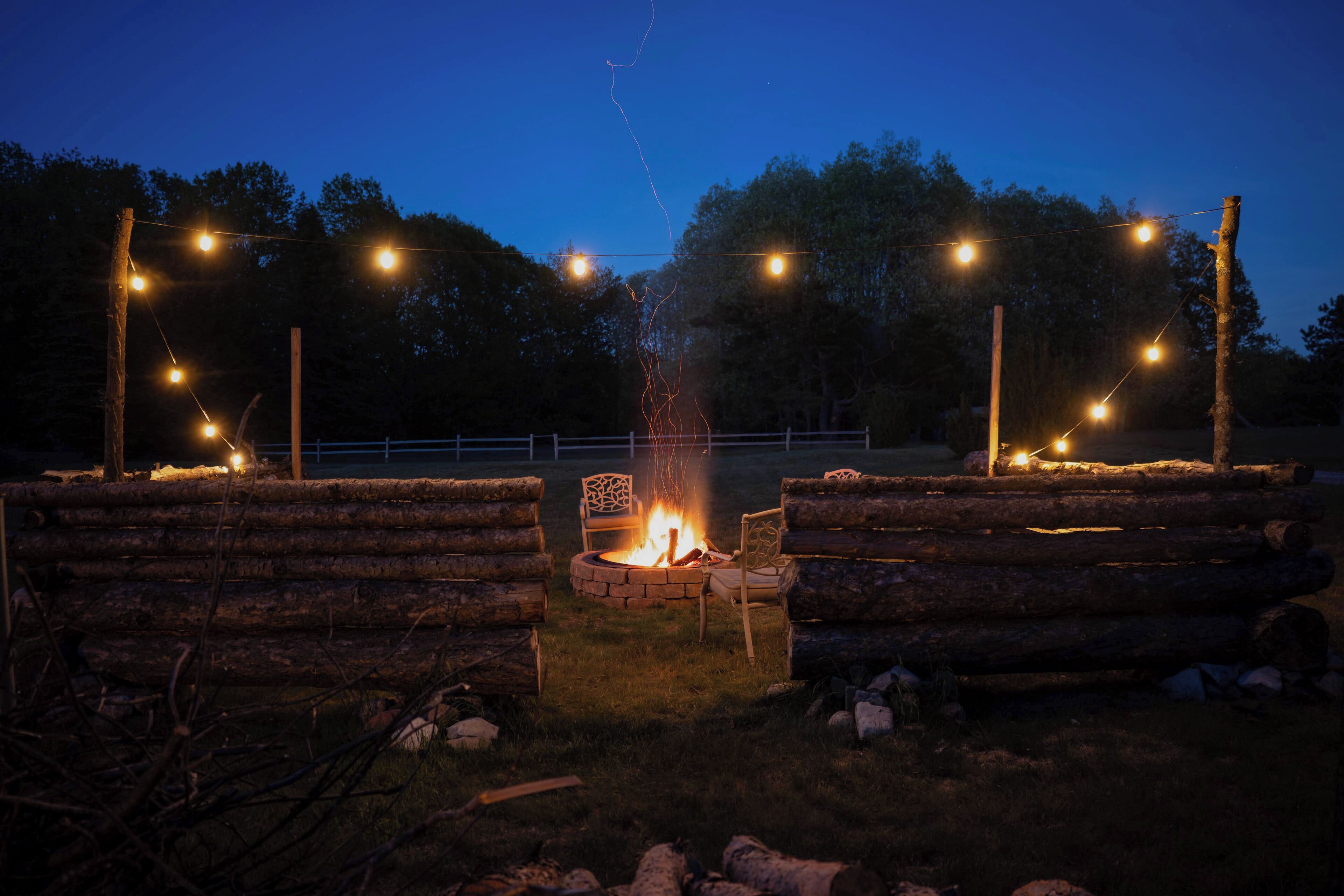 A campfire surrounded by logs, with string lights overhead.