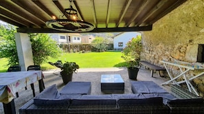 An outdoor patio with wicker furniture, a table with a floral tablecloth, and a stone wall. - Holiday home Carmen (Llanes)