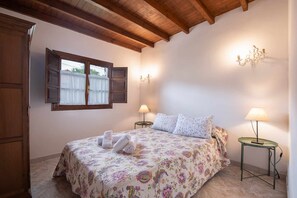 Ein Schlafzimmer mit einer blumigen Bettdecke, zwei Nachttischlampen, einer Holzboden und einem Fenster mit Vorhängen.