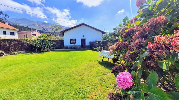 A white house with a red roof, a well-maintained lawn, and a garden with pink flowers. - Holiday home Carmen (Llanes)