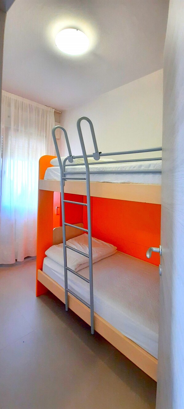 Una litera con escalera, una ventana con cortinas y una lámpara en el techo.