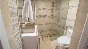 Un baño moderno con ducha envuelta en vidrio, inodoro blanco y tocador con espejo y toallero.