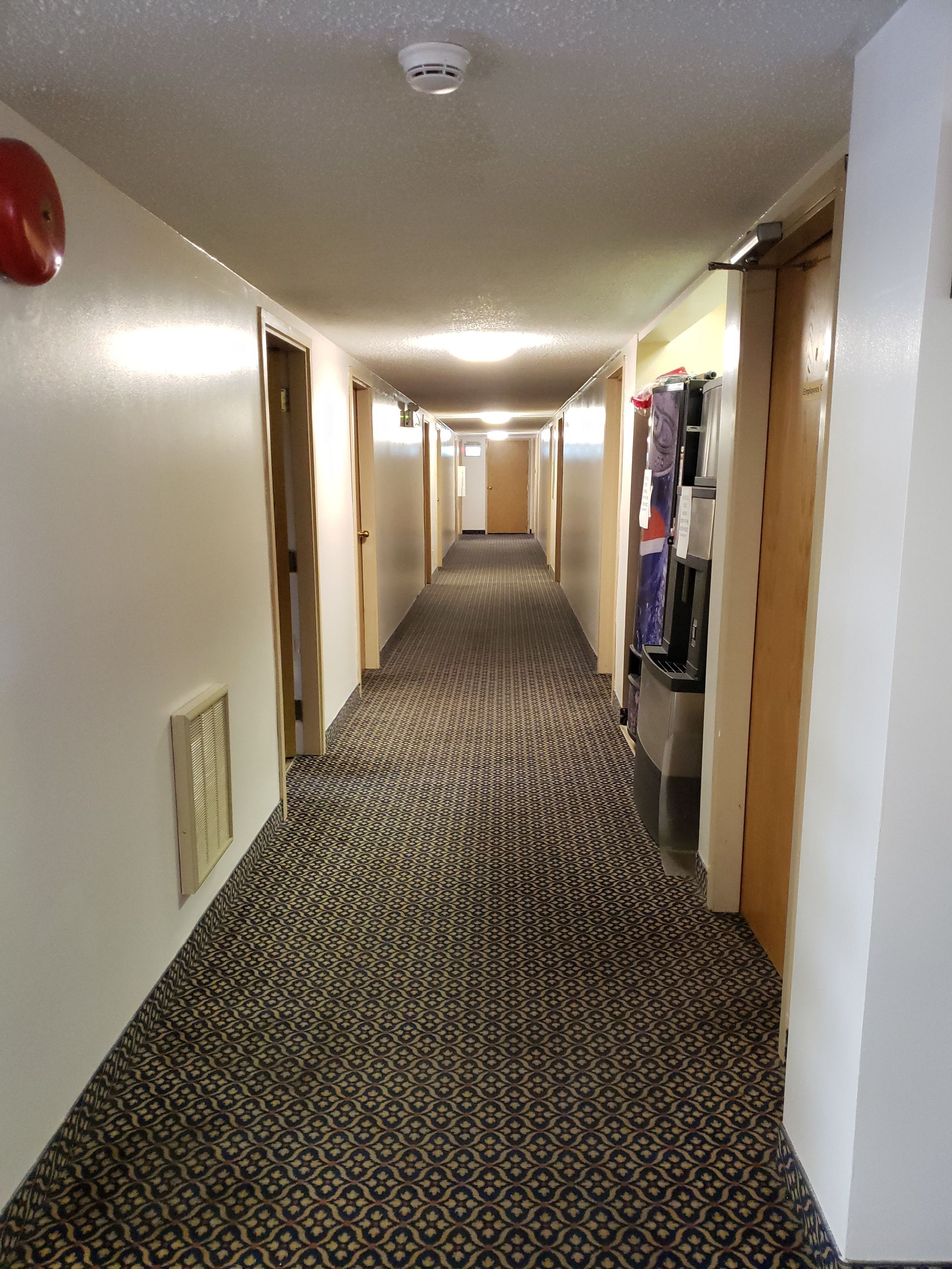 Un pasillo de hotel con alfombra estampada, puertas y una máquina expendedora.