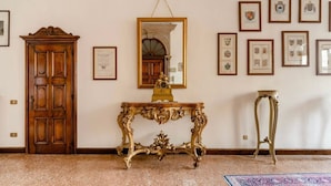 A room with a wooden door, a mirror, a gold ornate table, and framed pictures on the wall. - "LA FENICE" APARTMENT (Venezia)