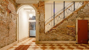 A hallway with a checkered floor, a red door, and a staircase with a wrought iron railing. - "LA FENICE" APARTMENT (Venezia)