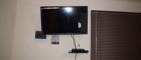 A television mounted on a wall with a power outlet and a cable management box below it.