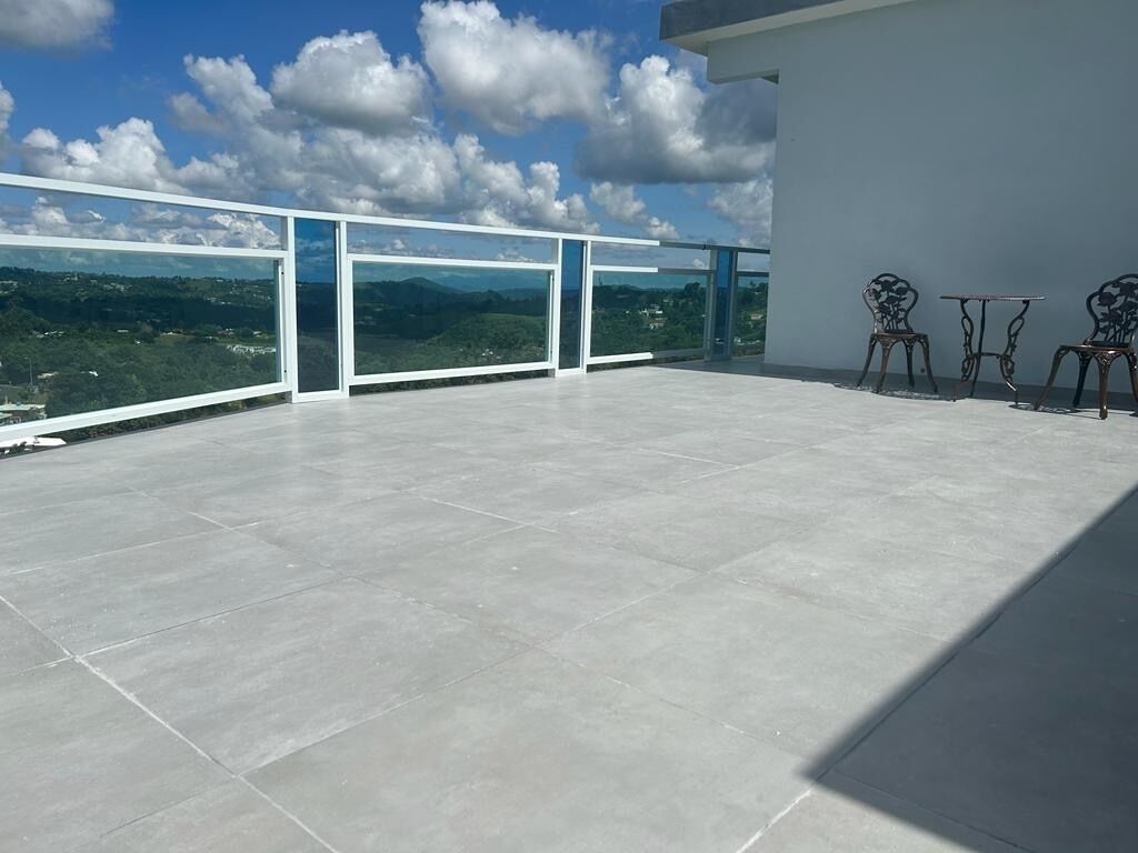 A spacious balcony with a clear view of the landscape, a glass railing, and a table with chairs.