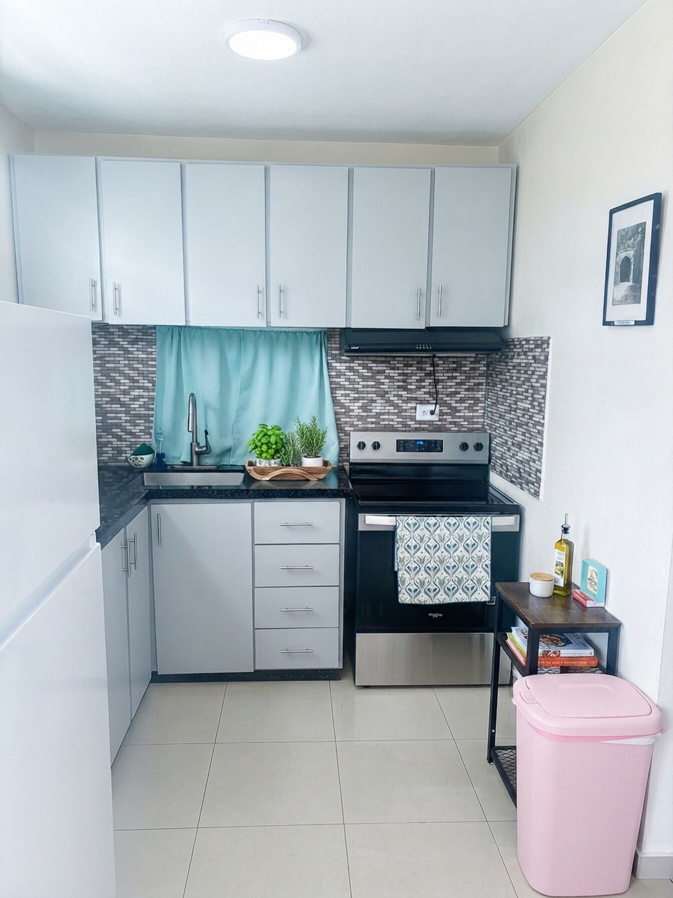 A compact kitchen with white cabinets, a black stove, and a small trash bin.