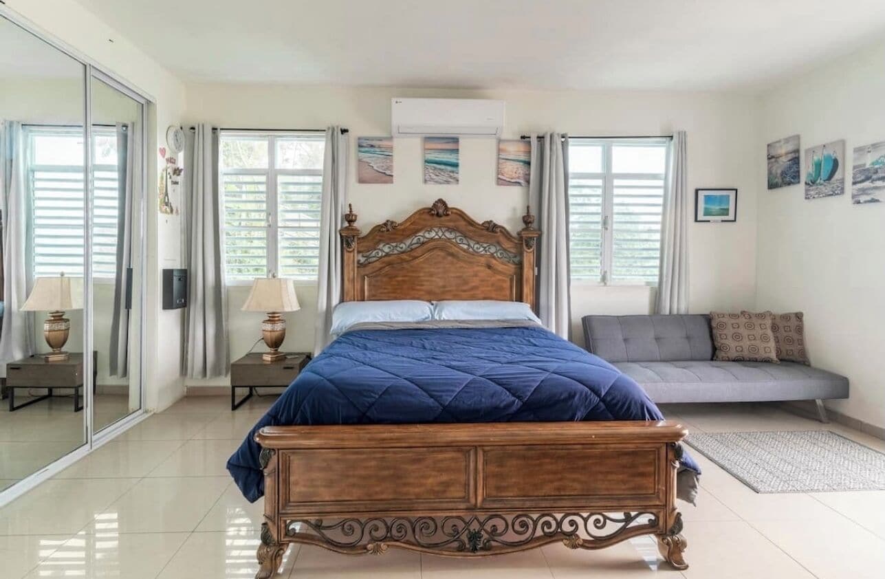 Een slaapkamer met een houten bed, een grijze bank en een groot raam met gordijnen.