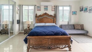 A bedroom with a wooden bed, a grey sofa, and a large window with curtains.