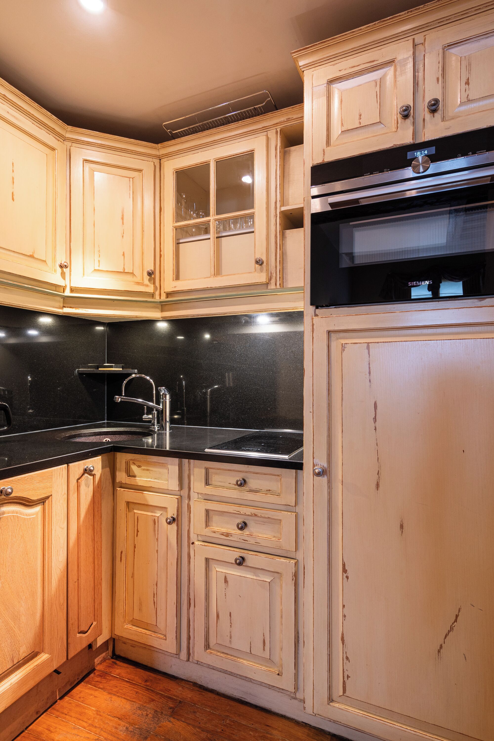 A kitchen with wooden cabinets, a black countertop, and a stainless steel oven.